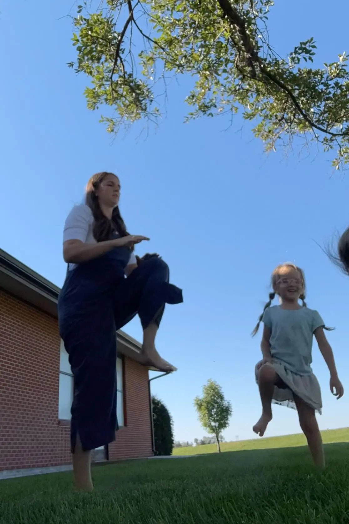 Mother and daughter enjoying an outdoor workout routine under a clear blue sky, doing a lively warm-up together on a grassy lawn. The image captures the fun and energetic vibe of a family-friendly workout routine.
